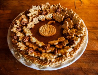 Homemade Pumpkin Pie Decorated with Pastry Cutouts of Autumn leaves with a center pumpkin, set on a wooden board with fresh pumpkins and pecans, selective focus