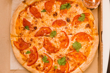 Delivery of delicious fresh hot pizza at home. Close-up Margarita with tomatoes, cheese and sauce in a box on the table