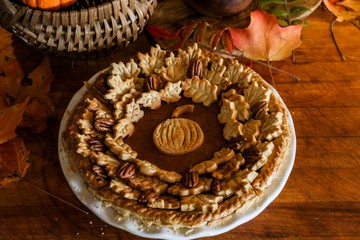 Homemade Pumpkin Pie Decorated with Pastry Cutouts of Autumn leaves with a center pumpkin, set on a wooden board with fresh pumpkins and pecans, selective focus