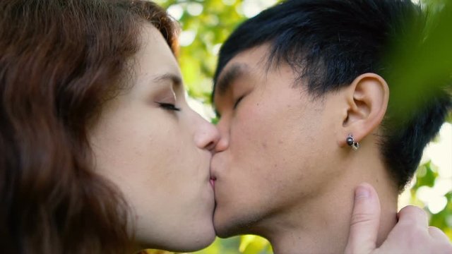 Mixed Ethnicity Asian Caucasian Couple Kissing Passionately Below Tree in Nature During Sunset