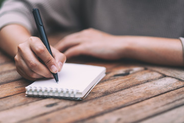 Closeup image of a woman writing on blank notebook on wooden table