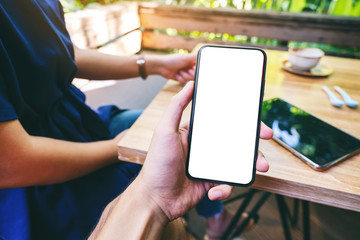 Mockup image of a man holding black mobile phone with blank white screen with woman drinking coffee in cafe