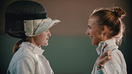Two young and beautiful fencers in helmet are looking at each other and smiling