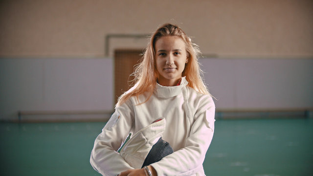 Young fencer is holding in hands a helmet and looking at the camera