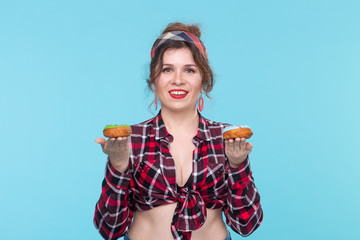 Positive young pin-up girl model holding in hands multicolored donuts posing on a blue background. Cooking concept for desserts and sweets.