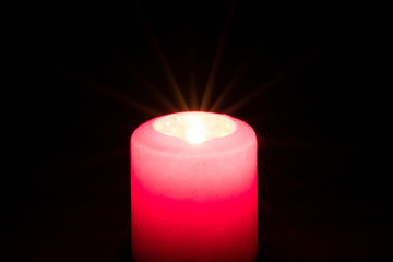 Brennende rote Kerze als Weihnachtskerze oder Weihnachtsdekoration erleuchtet die Dunkelheit und schwarze Nacht in der Adventszeit
