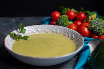 Detox green broccoli cream soup with chia seeds, red onions, green peppers, cherry tomatoes and croutons on a gray background. Healthy eating concept. Copy space. 