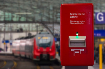 A platform in a train station in Berlin. Tickets have to be pushed in on a red machine. The English translation is on the machine: Ticket please validate here.