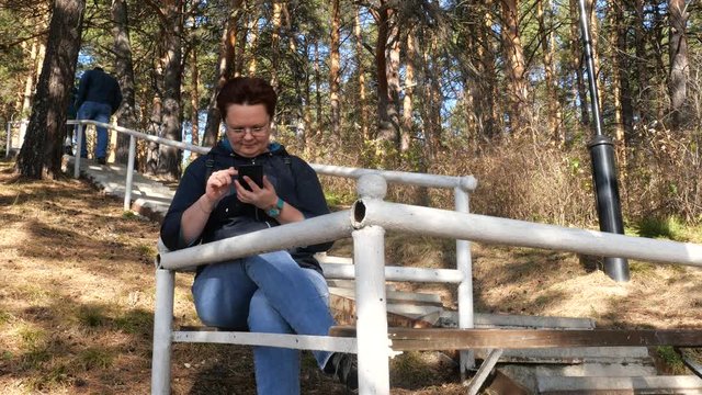 A woman sits on a bench and looks into a smartphone.