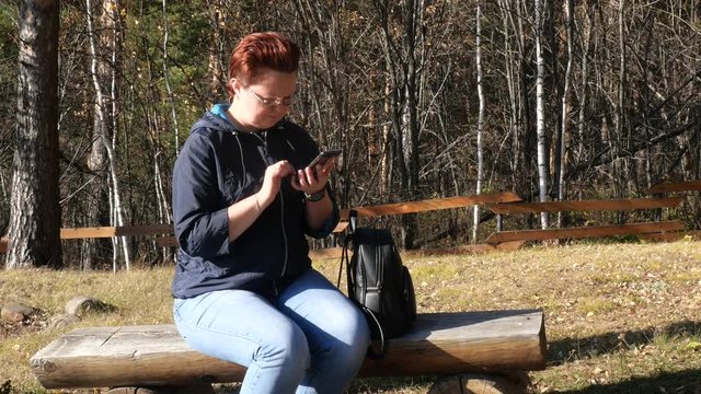 A woman sits on a bench and looks into a smartphone.