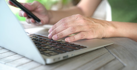 Woman's hands busy typing on keyboard and cell phone.