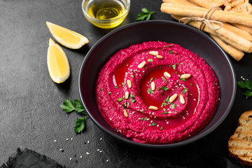 Baked Beet Hummus with toasted bread  in a black ceramic bowl on a dark background. Top view