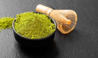Green matcha tea powder in black bowl.