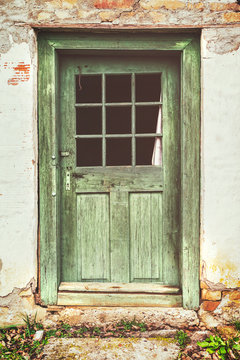 An old rotten wooden door on crumbling house. Vintage matte look effect.
