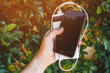 Hand holding mobile phone with charging power bank, recharging smartphone