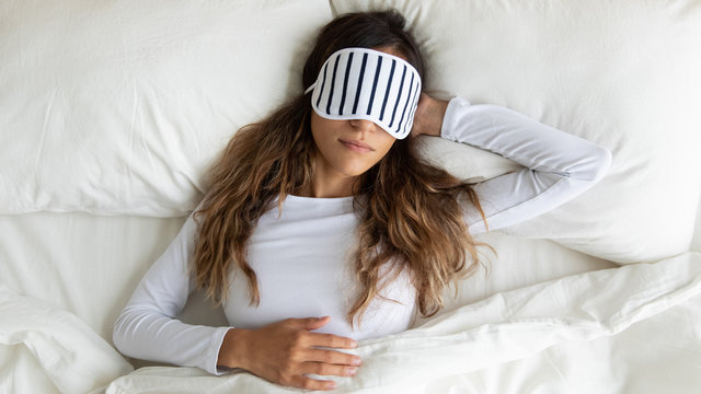 Calm peaceful mixed race young lady wearing sleeping mask, dreaming.