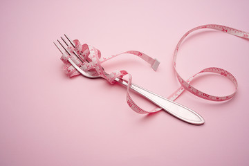 Fork and spoon tied with a pink measuring tape on a pink background : healthy diet concept.