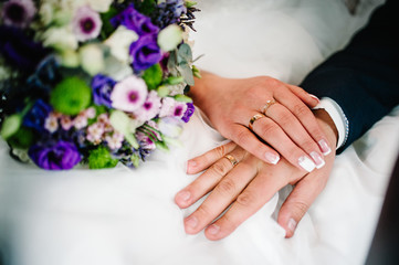 Hands are newlyweds with wedding rings. Close up. On the background of a wedding bouquet of flowers.