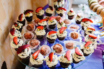 cupcakes with cream and strawberries. Cake, Pie, Fruit cakes, muffins, nuts on a glass surface on the plate. Dessert. The sweetness. Gentle tone. Against the background of sweets. Close up
