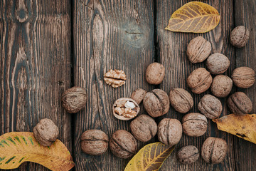 Autumn harvest background. Walnut kernels and whole walnuts with yellow leaves on rustic old wooden table. Flat lay.