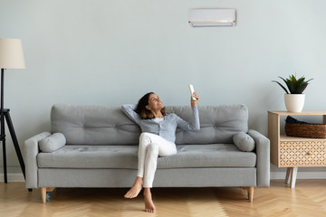Joyful mixed race woman turning on cooler system air conditioner.