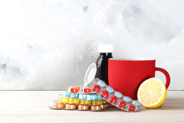 Bottles of cough syrup, cup of hot tea, lemon, honey and different pills on background