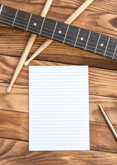 Blank notepad with guitar and drum stick on wooden background.