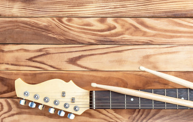 Guitar with drum sticks on wooden background.