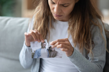 Stressed girl tearing photo with boyfriend or husband in half.