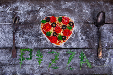 Heart shaped pizza ingredients. The name of the pizza is written in arugula.