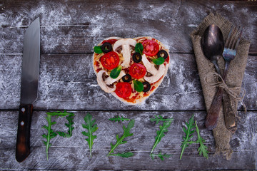 Heart shaped pizza ingredients. The name of the pizza is written in arugula.