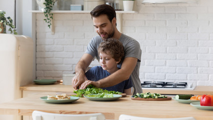 Caring father teaching little son top use knife in kitchen