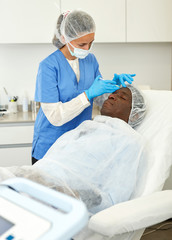 Female doctor examining skin of patient before facial procedure in clinic