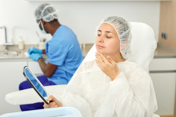 Female client looking to mirror before mesotherapy in esthetic  cosmetology  clinic