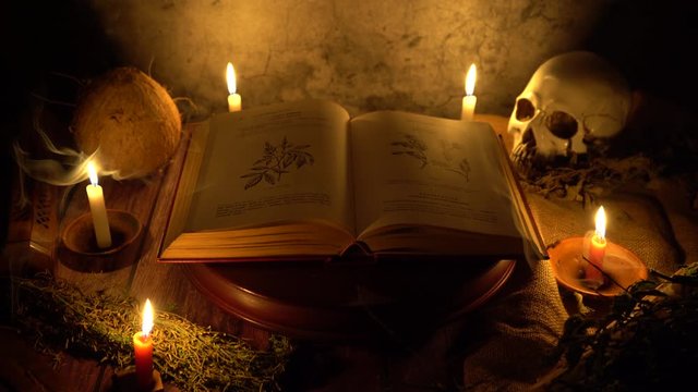 Front view of an old herbal medicine book on a wooden platform with candles and a skull behind