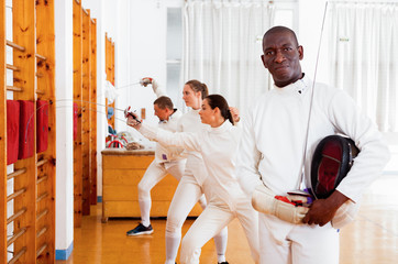 Active african american male fencer in uniform standing with mask and foil at fencing room