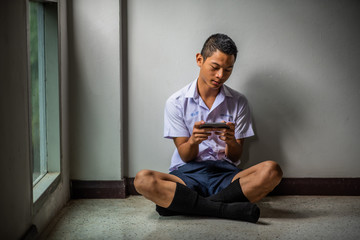Male Asian high school student in white uniform addicted to online games.