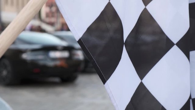 Modern luxury cars stand at the exhibition against the backdrop of a black and white racing flag.