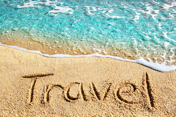 Word TRAVEL written on yellow sand, blue sea wave, white foam top view close up, handwriting letters text, ocean water, summer holidays concept, vacations on paradise tropical beach banner, copy space