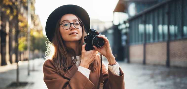 Hobby photographer concept. Outdoor lifestyle portrait of pretty young woman in sun city in Europe with camera travel photo of photographer in glasses and hat take photo copy space mockup