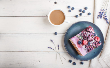 Berry cake with milk cream and blueberry jam on blue ceramic plate with cup of coffee and fresh blueberries on a white wooden background. top view.