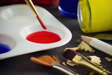 Closeup artist paint brush above color plate and poster color bottle on table. Concept of art...