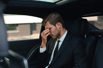 Tired overworked businessman dressed in full suit massaging nose while sitting in the car.