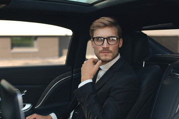 Fototapeta na wymiar Thoughtful confident businessman in full suit with eyewear looking away while sitting in the car.