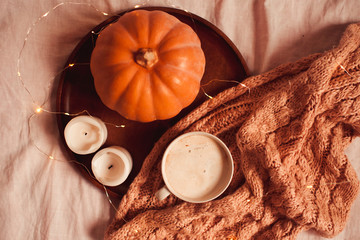 Cup of tasty latte, burning candles, fresh pumpkin and knitted scarf in bed closeup.