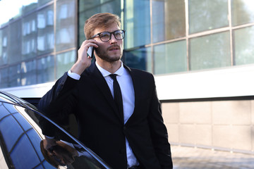 Handsome serious young businessman standing near his comfortable new car and going to the office.