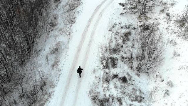 Aerial view of the man walking through the winter forest