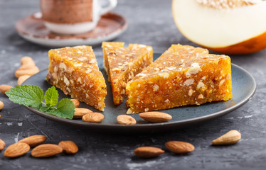 Traditional turkish candy cezerye made from caramelised melon, roasted walnuts, cashew, pistachios in blue ceramic plate and a cup of coffee on a black concrete background. side view, selective focus.