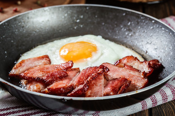Slices of smoked bacon and fried egg in frying pan
