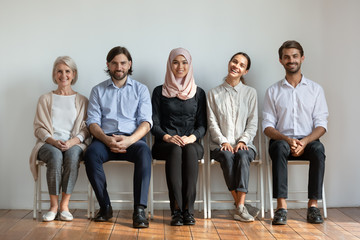 Smiling multicultural professional business people sit on chairs in row